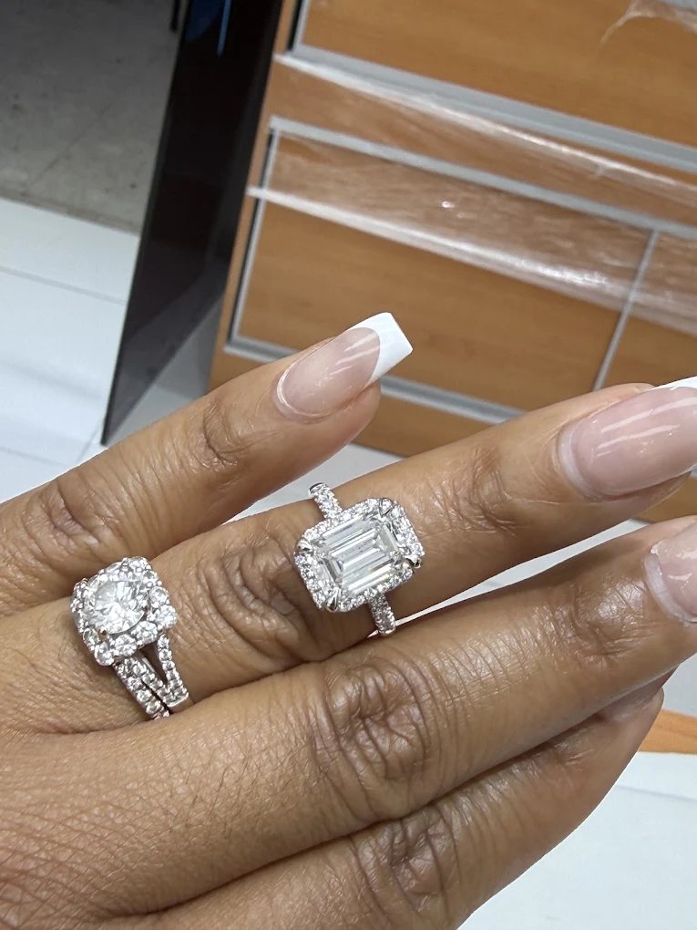 A customer's hand wearing a cushion halo bridal set and an emerald cut halo engagement ring